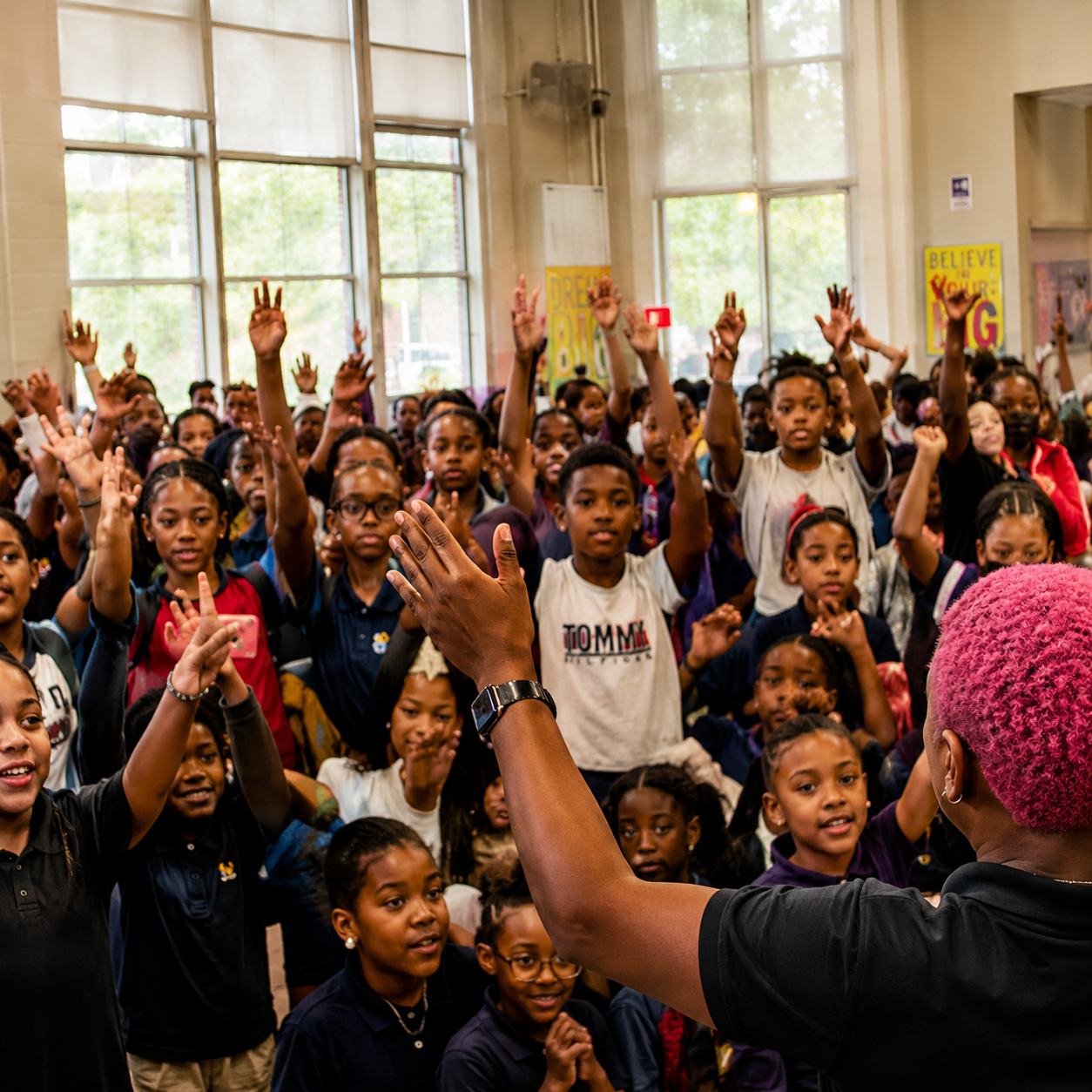 Kina Evans leading a Bully Talk Inc. school assembly, students with hands raised