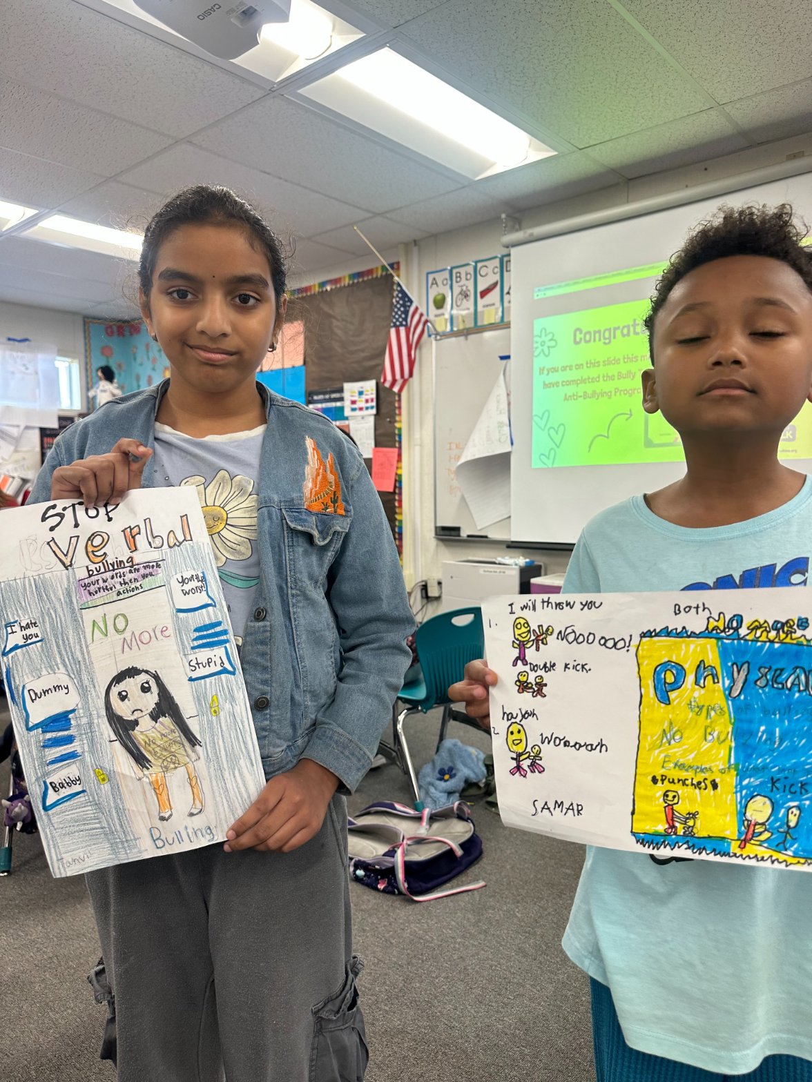 Two elementary students holding their hand-drawn anti-bullying posters